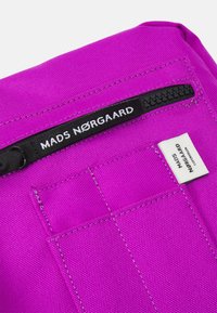 Fuchsiová texturovaná látková příslušenství s černým zipem a bílou štítkou. Obsahuje logo visačku a prošívané detaily na povrchu.