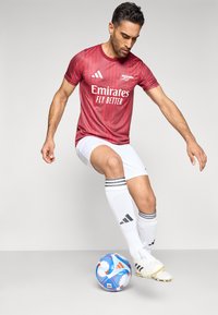 Rode voetbalshirts met verticale strepen, witte korte broek en zwart-wit gestreepte sokken. Adidas-logo en "Emirates Fly Better" weergegeven.