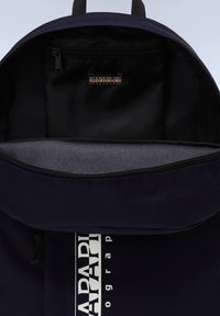 Zaino blu navy con apertura a zip, caratterizzato da una tasca interna nera e un logo bianco sul davanti. Realizzato in tessuto resistente.