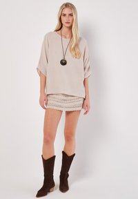 Beigetexturerad topp med avslappnade ärmar, matchad med en ljusbeige minikjol med spetsdetaljer och mörkbruna mockakängor i knähöjd.