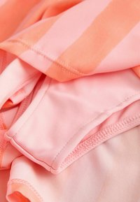 Gros plan d’un tissu doux plié avec un motif rayé pêche et rose et des coutures détaillées.