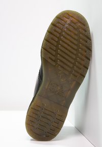 Suola nera della scarpa con un motivo di grip in gomma testurizzata, caratterizzata da un bordo marrone chiaro e un logo e dettagli in rilievo sul fondo.