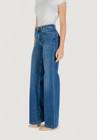 Højtaljede, vide bukser i middelblå denim med en glat tekstur og diskret syninger. Har et klassisk fem-lommer design.