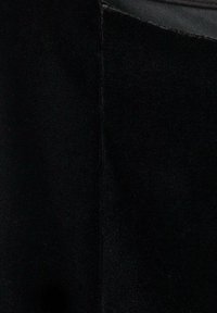 Czarny materiał z pionowym przeszyciem i teksturowanym pasem w górnym prawym rogu.