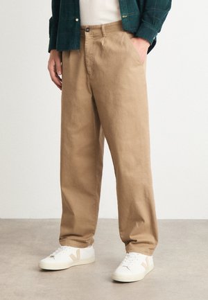 Beige straight-leg trousers made of cotton twill, featuring side pockets and a button closure, paired with white sneakers.