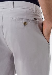 Pantaloni in cotone grigio chiaro con una texture liscia, dotati di un singolo bottone sulla tasca posteriore e di un'etichetta del marchio discreta.