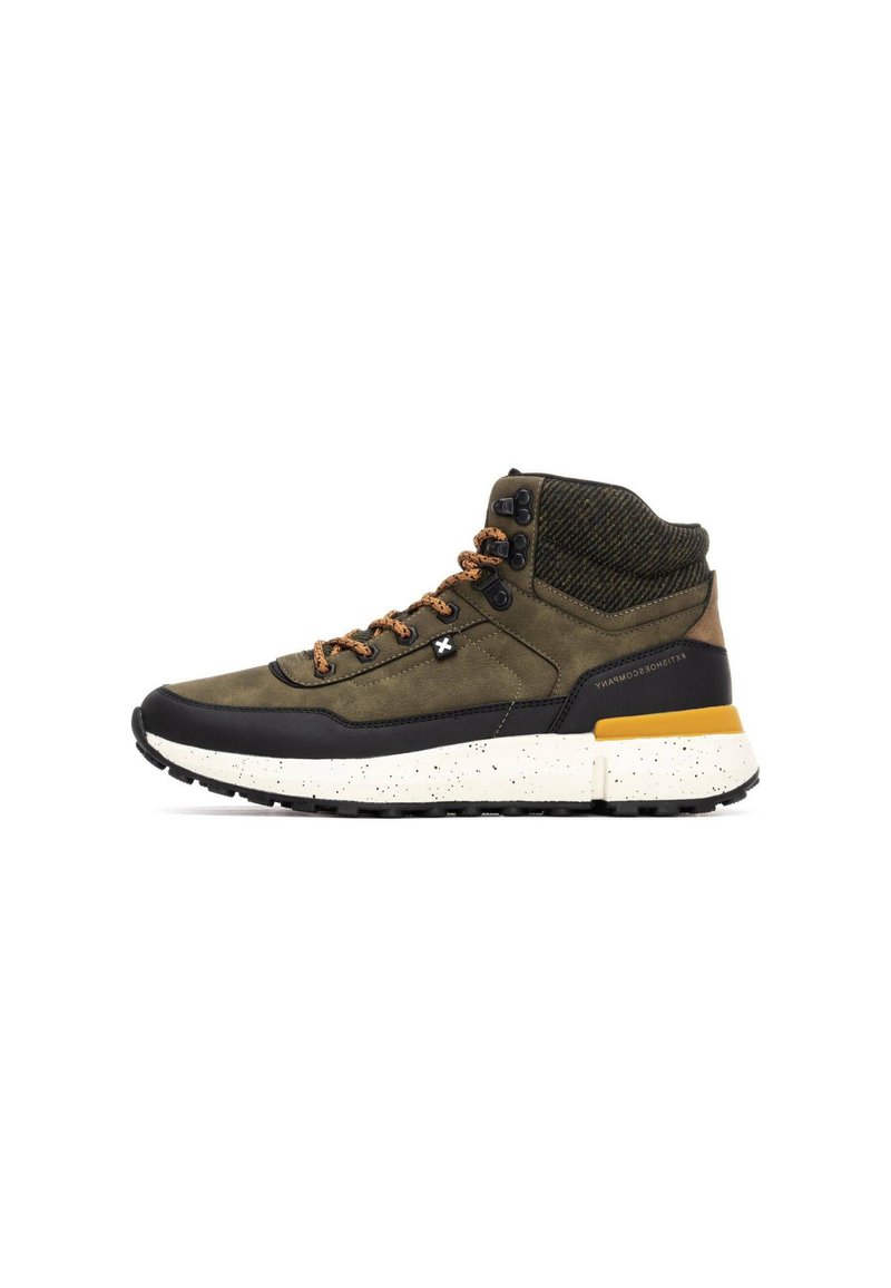 Zapatilla alta en verde oliva y negro, con tejido texturizado, cordones marrones y una suela blanca moteada con un acento amarillo.