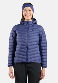 Marineblaue, isolierte Steppjacke mit horizontalen Nähten, Reißverschluss und Kapuze. Kombiniert mit schwarzen Hosen, die ein schlankes Design zeigen.