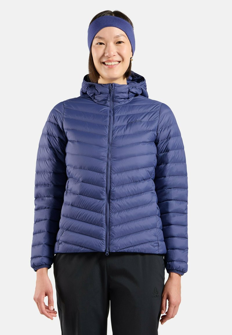 Marineblaue, isolierte Steppjacke mit horizontalen Nähten, Reißverschluss und Kapuze. Kombiniert mit schwarzen Hosen, die ein schlankes Design zeigen.