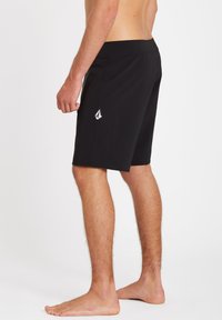 Shorts de bain noirs en tissu léger, avec une taille flexible et un petit logo brodé sur le côté gauche.