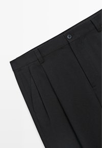 Pantalon noir ajusté avec des plis, passants de ceinture, poches latérales et fermeture à bouton à la taille.