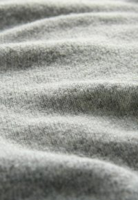 Tejido gris con una superficie suave y texturizada, que muestra arrugas sutiles y un patrón uniforme. Ligero, con una apariencia acogedora.