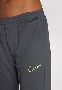 Gray athletic pants made from textured fabric. Features an elastic waistband and a neon green Nike logo on the left side.
