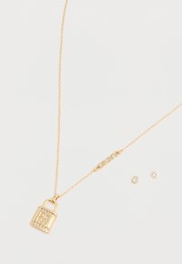 Collana d'oro con pendente a forma di lucchetto e incisione "DKNY" e due piccoli perni con gemme trasparenti, presentata su uno sfondo chiaro.