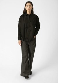 Black button-up shirt with decorative bows on sleeves, paired with gray wide-leg trousers, both featuring structured designs and smooth textures.