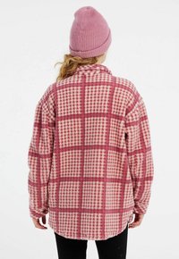 Vaaleanpunainen ja kerma ruudullinen flanellipaita, jossa on pehmeä tekstuuri ja pyöristetty helma. Yhdistetty samanväriseen vaaleanpunaiseen neulottuun pipoon.