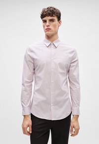 Lichtroze overhemdd met smalle witte strepen, klassieke kraag en lange mouwen. De stof lijkt glad en iets getailleerd.