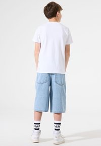 T-shirt blanc à manches courtes, shorts en jean bleu clair à la coupe décontractée, baskets blanches et chaussettes rayées noir et blanc.