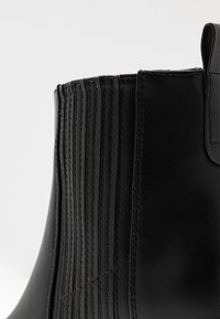 Czarne skórzane botki za kostkę z pionowym ryflowaniem, gładką teksturą i akcentami w postaci przeszyć. Posiadają pętelkę ułatwiającą zakładanie.