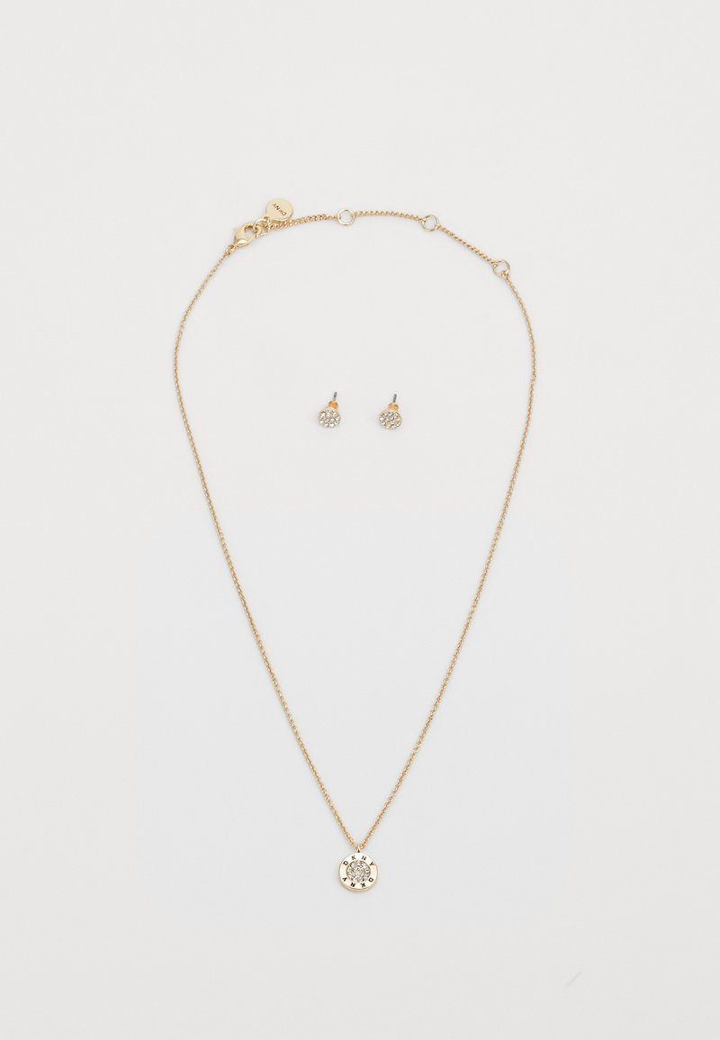 Kuldtooni kaelakee ringikujulise ripatsiga, millel on põhjalik disain ja väikesed kivid, koos sobivate stud-kõrvarõngastega.