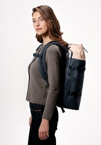 Batoh vyrobený z navy modrého materiálu, se skládacím vrchem, nastavitelnými popruhy a světle růžovým vrchem. Obsahuje přezky a strukturovanou tkaninu.