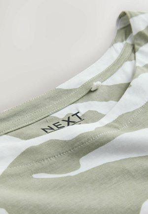 Prim-plan al unei guler de haină cu dungi verzi și albe, cusături vizibile și eticheta neagră a brandului NEXT în interior.