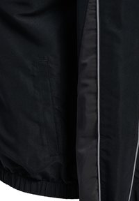 Czarna kurtka o błyszczącej fakturze, z elastycznym pasem, boczną kieszenią oraz kontrastującym szarym obszyciem wzdłuż przednich krawędzi.