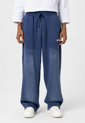 Blauwe sweatpants van zachte stof, met een elastische tailleband met een trekkoord en een wit logo op de linkerdij. Losse pasvorm.