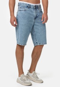 Shorts en denim bleu clair avec une coupe décontractée, un design à cinq poches et des ourlets roulés. Portés avec des baskets de sport grises.
