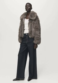 Graue Jacke aus Kunstpelz mit breitem Kragen, kombiniert mit hoch taillierter, weiter Jeans im Dunkelblau und einem weißen Tanktop.