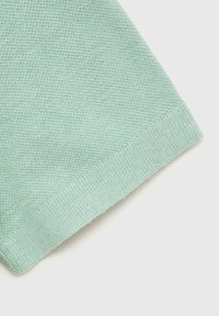 Tessuto di un verde chiaro con una texture a nido d'ape, caratterizzato da un orlo a costine e una finitura morbida e leggermente pelosa.
