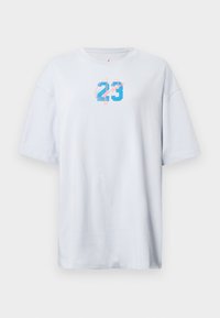 Biely oversized tričko vyrobené z bavlny, s modrým číslom "23" a ružovým písmom. Krátke rukávy a okrúhly výstrih. Hladká textura.
