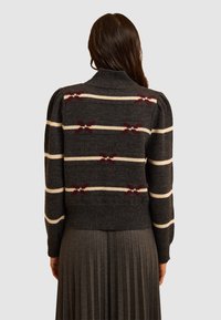 Maglione grigio a maglia con colletto alto, caratterizzato da strisce bianche e motivi a fiocco bordeaux. L'orlo a costine e le maniche a sbuffo aggiungono texture.