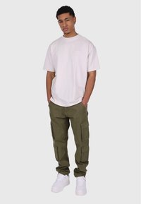 Camiseta blanca de cuello redondo, pantalones cargo verde oliva con bolsillos laterales y zapatillas blancas. Ajuste casual y textura de tela resistente.