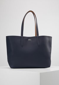 Sac fourre-tout bleu marine avec deux poignées, finition texturée et petit logo crocodile argenté centré sous les poignées.