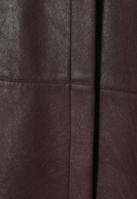 Tessuto in pelle bordeaux con superficie tessurizzata, caratterizzato da cuciture definite e una finitura liscia che mette in risalto la sua morbida lucentezza.