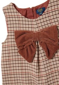 Robe à carreaux avec un nœud en velours marron au niveau du col. Fabriquée en mélangé de coton avec une texture douce. Les couleurs incluent beige, bordeaux et marron.