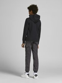 Felpa nera con cappuccio, pantaloni cargo grigi, sneakers bianche. La felpa presenta un grande cappuccio; i pantaloni hanno molte tasche e polsini elasticizzati.