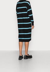 Vestito a maglia a strisce nere con strisce orizzontali azzurre chiaro, maniche lunghe e vestibilità comoda, che arriva a metà polpaccio, indossato con scarpe nere.