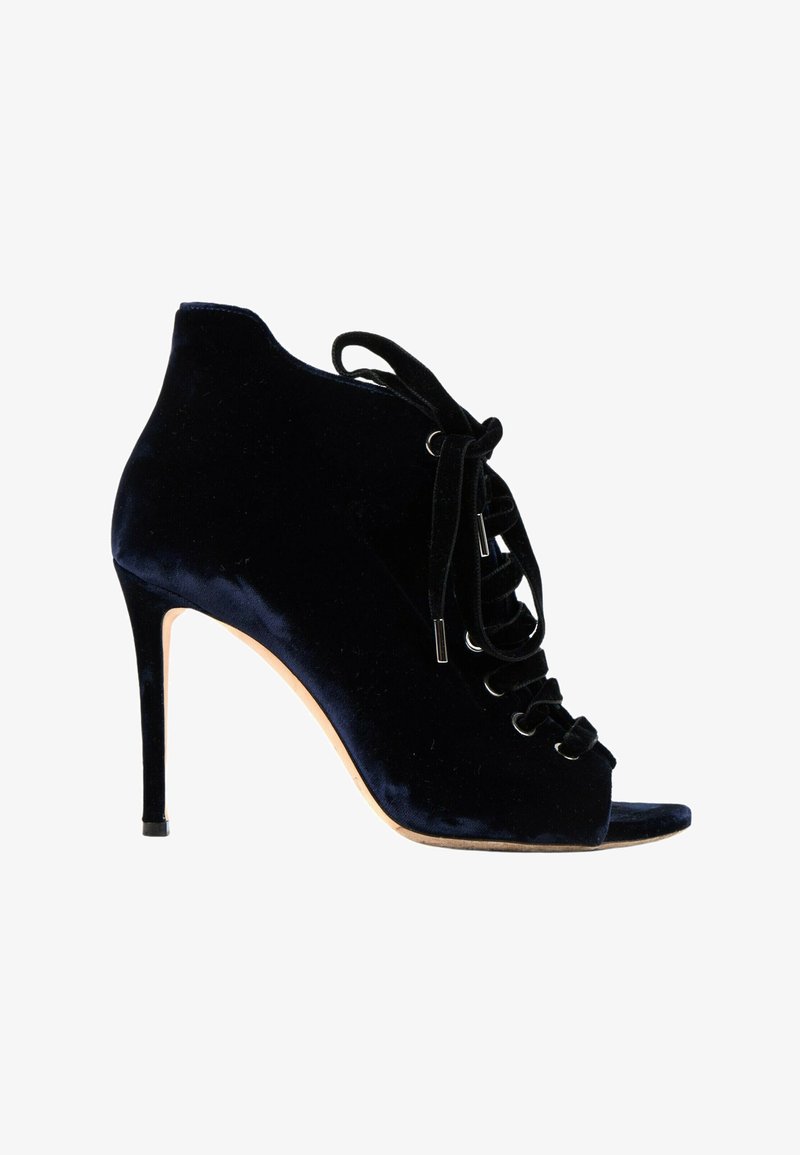 Bottine en velours noir à talon haut, lacets à l’avant et bout ouvert, semelle beige et talon aiguille sur fond blanc.