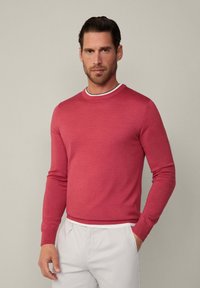 Roter Pullover mit langen Ärmeln und Rundhalsausschnitt, mit einem weißen und schwarzen gestreiften Akzent am Kragen. Glatte Strickstruktur.
