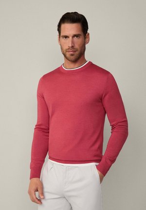 Roter Pullover mit langen Ärmeln und Rundhalsausschnitt, mit einem weißen und schwarzen gestreiften Akzent am Kragen. Glatte Strickstruktur.