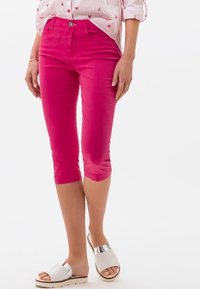 Pantalones cortos de algodón en un brillante color rosa, con un diseño ajustado, bolsillos laterales y cierre de botón. Se combinan con sandalias blancas con un acento plateado.