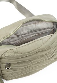 Bandolera acolchada beige con cremallera abierta que revela compartimentos interiores acolchados y correa para el hombro ajustable.