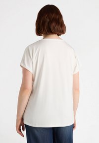 Camiseta blanca de manga corta con cuello redondo, textura suave y ajuste relajado; combinada con jeans de mezclilla oscura.