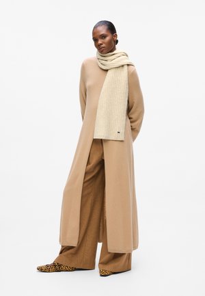 Long beige coat over taupe wide-leg trousers, paired with a cream ribbed scarf. Features black and leopard-print pointed flats. Simple, elegant design.