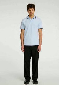 Šviesiai mėlynas polo marškinėlis su įmegztu apykakle, juodais akcentais ir trumpomis rankovėmis; derinamas su juodomis kelnėmis ir batais.