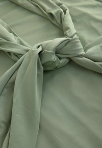 Hellgrüner Stoff mit glatter Textur und einem gedrehten Knotendetail. Der Hintergrund besteht aus einem ähnlich weichen grünen Material.