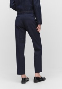 Marineblauwe gestreepte broek met een slim fit, gemaakt van een soepele stof. Beschikt over schuine achterzakken en een cropped lengte. Zwarte loafers gedragen.