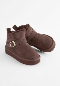Bruna mocka ankle boots med fuskpälsfoder, en platt gummisula och en spänneaccent på sidan. Texturerad ovandel för extra detalj.